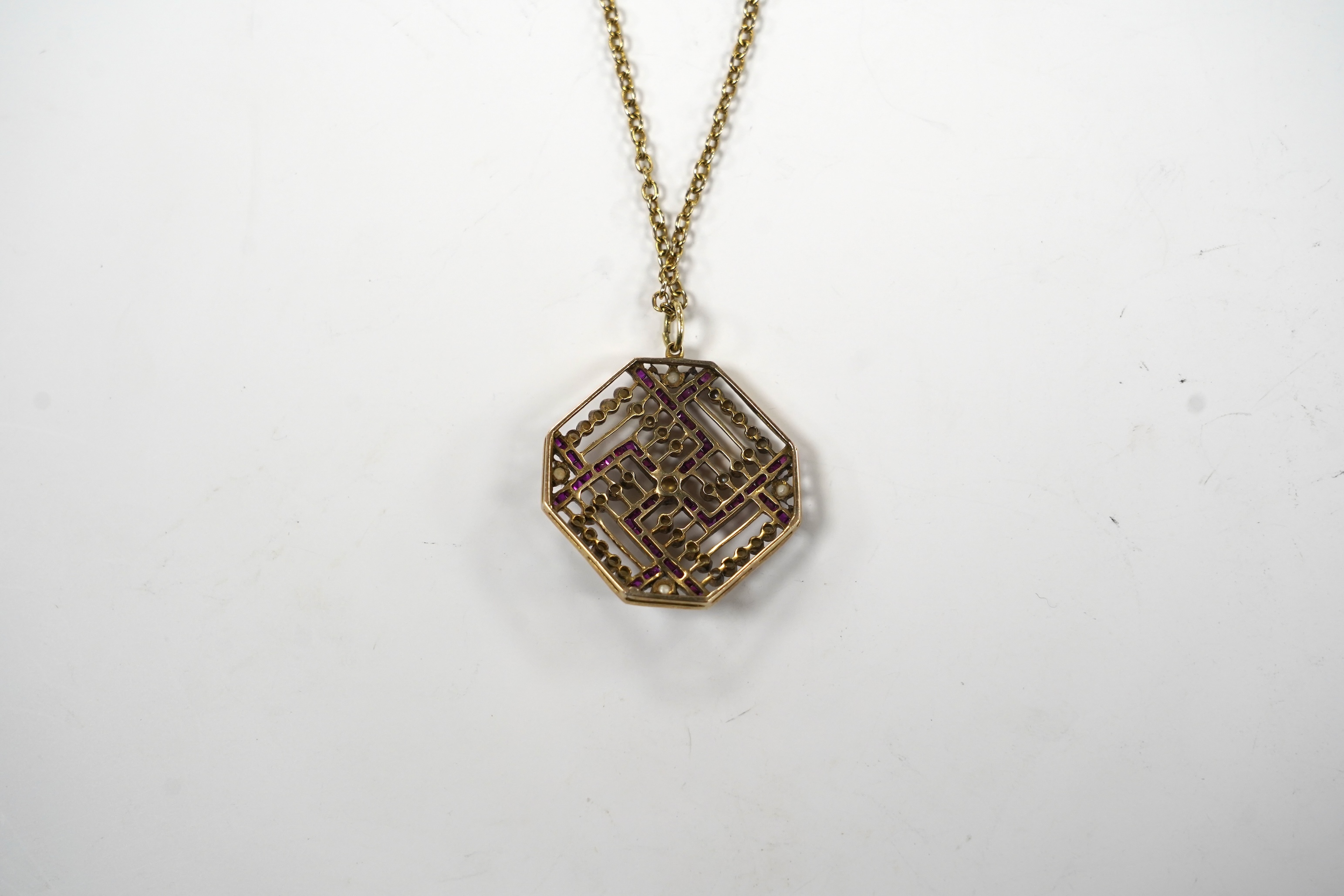 An Edwardian 15ct, ruby and seed pearl set octagonal pendant, 35mm, gross weight 9.7 grams, on a gilt metal chain.